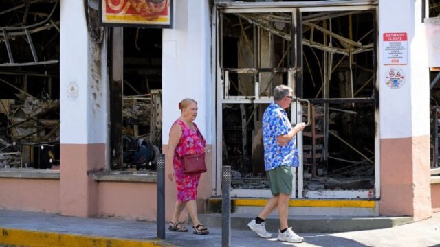 tourists-walk-past-a-burned-shop.jpg